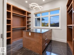 Built-in wood-finish shelving and hanging rods, central island with drawers and a dark countertop, elegant chandelier, recessed lighting, and large multi-pane window - 