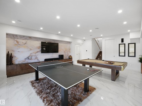 Recessed lighting, large format tile flooring, built-in media console, accent wall with patterned finish, and a staircase with wood-finish treads - 4809 Woolsey Lane Nw, Edmonton, AB 