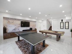 Recessed lighting, large format tile flooring, built-in media console, accent wall with patterned finish, and a staircase with wood-finish treads - 