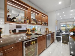 Built-in wet bar featuring a beverage refrigerator, integrated sink, dishwasher, and wood-finish cabinetry with accent lighting - 