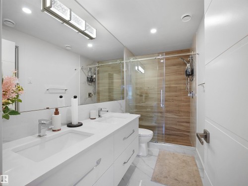 Double vanity with integrated sinks, recessed lighting, wood-finish shower wall, glass-enclosed shower, and a full-width vanity mirror - 4809 Woolsey Lane Nw, Edmonton, AB 