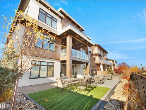 Multi-level exterior featuring a combination of light-toned stucco and wood-finish siding, multiple balconies with glass railings, a stone patio, and artificial turf sections - 4809 Woolsey Lane Nw, Edmonton, AB 