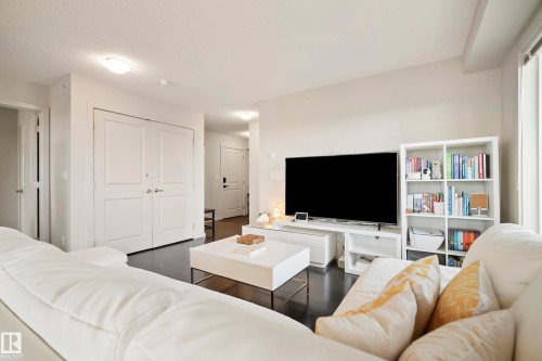 Spacious living area featuring dark wood-finish flooring, white walls, and bright overhead lighting - #419 5515 7 Av Sw, Edmonton, AB 