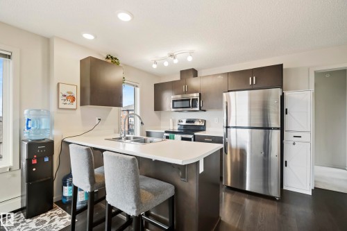 Kitchen with dark wood-finish cabinetry, stainless steel appliances, a center island with a sink, and recessed lighting - #419 5515 7 Av Sw, Edmonton, AB 