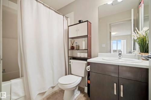 Bathroom featuring a white bathtub, a toilet, a vanity with a white countertop and dark cabinetry, a wall-mounted mirror, and overhead lighting - #419 5515 7 Av Sw, Edmonton, AB 
