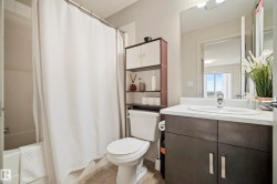 Bathroom featuring a white bathtub, a toilet, a vanity with a white countertop and dark cabinetry, a wall-mounted mirror, and overhead lighting - 