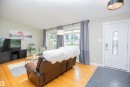 Light wood-finish flooring, entry with dark tile flooring, white paneled entry door with decorative glass, and a contemporary ceiling light fixture - 9107 58 Street Nw, Edmonton, AB 