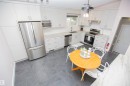 Kitchen featuring extensive white cabinetry, light-toned countertops, integrated stainless steel appliances, dark tile flooring, and a contemporary light fixture - 9107 58 Street Nw, Edmonton, AB 
