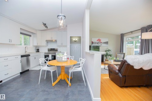 Light-toned kitchen cabinetry with stainless steel appliances, a tile backsplash, and a contemporary pendant light fixture - 9107 58 Street Nw, Edmonton, AB 