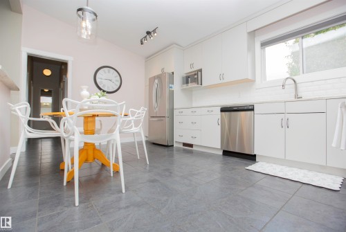Kitchen featuring stone-look floor tiles, white shaker-style cabinetry, and stainless steel appliances - 9107 58 Street Nw, Edmonton, AB 
