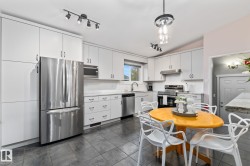 Kitchen featuring extensive white cabinetry, light-toned countertops, integrated stainless steel appliances, dark tile flooring, and a contemporary light fixture - 
