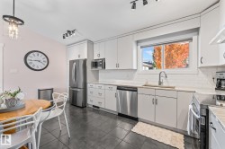 Light-toned kitchen cabinetry with stainless steel appliances, a tile backsplash, and a contemporary pendant light fixture - 