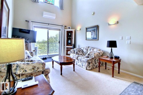 Vaulted ceiling with high windows, sliding glass door, wall-mounted air conditioning unit, and wall sconces - #421 592 Hooke Rd Nw, Edmonton, AB 