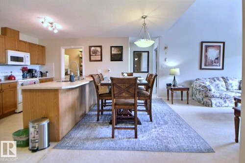 Kitchen with wood-finish cabinetry, white appliances, and a peninsula countertop - #421 592 Hooke Rd Nw, Edmonton, AB 