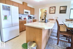 Kitchen featuring wood cabinetry, white appliances, light-toned countertops, and a kitchen island with an integrated sink - 