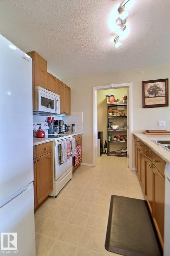 Kitchen featuring wood-finish cabinetry, a freestanding range, and a built-in microwave - #421 592 Hooke Rd Nw, Edmonton, AB 