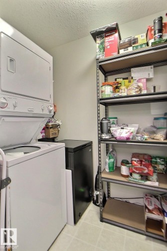 Laundry area with a white stackable washer and dryer, a black compact freezer, and metal shelving - #421 592 Hooke Rd Nw, Edmonton, AB 