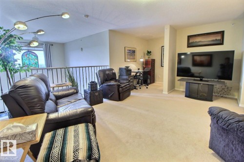 Open concept living space with carpeted flooring, a dedicated office area, and interior railing - #421 592 Hooke Rd Nw, Edmonton, AB 