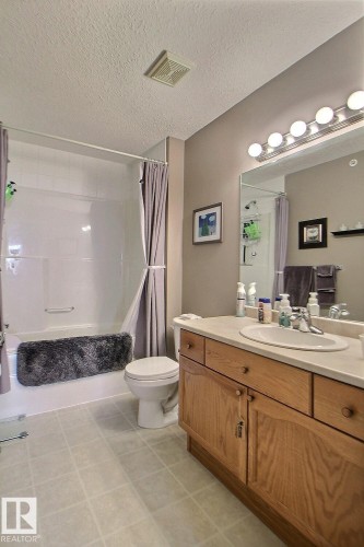 Tub-shower combination with white tile surround, wood-finish vanity with countertop, and integrated sink - #421 592 Hooke Rd Nw, Edmonton, AB 