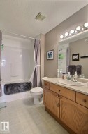 Tub-shower combination with white tile surround, wood-finish vanity with countertop, and integrated sink - 
