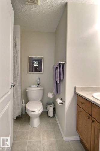 Tile flooring, white toilet, single-door vanity with a light-toned countertop, and a shower with a curtain rod - #421 592 Hooke Rd Nw, Edmonton, AB 
