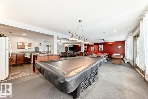 Entertainment area featuring a pool table, overhead lighting, an adjacent kitchen, and a dining space with red accent walls - #421 592 Hooke Rd Nw, Edmonton, AB 