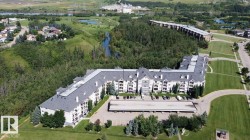 Multi-story building featuring dormer windows, covered parking, and an expansive paved lot - 