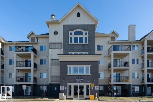 Multi-story building with a central entrance featuring glass doors, balconies with black railings, and varied exterior siding - #421 592 Hooke Rd Nw, Edmonton, AB 