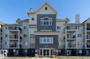 Multi-story building with a central entrance featuring glass doors, balconies with black railings, and varied exterior siding - #421 592 Hooke Rd Nw, Edmonton, AB 