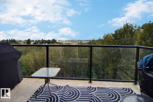 Balcony with glass panel railing and concrete flooring overlooking a wooded area - #421 592 Hooke Rd Nw, Edmonton, AB 
