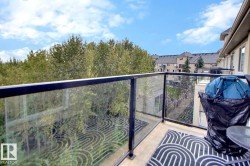 Balcony with glass panel railing and metal frame, offering an elevated perspective of mature trees and surrounding residential structures - 