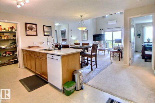 Kitchen island with integrated sink, light wood-finish cabinetry, and a built-in dishwasher - #421 592 Hooke Rd Nw, Edmonton, AB 