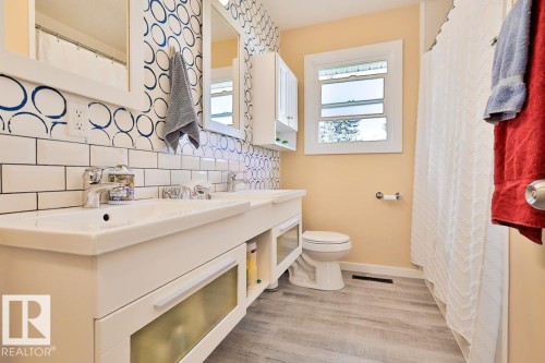 Dual vanity with integrated sinks, subway tile backsplash, wood-finish flooring, and a white framed window - 13312 123A Street Nw, Edmonton, AB 