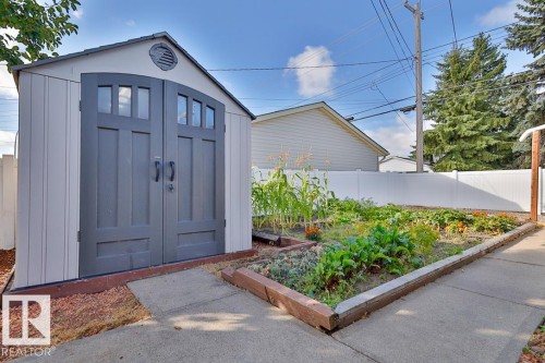 Storage shed with arched double doors, white vinyl fencing, and a garden bed with concrete edging - 13312 123A Street Nw, Edmonton, AB 