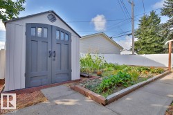 Storage shed with arched double doors, white vinyl fencing, and a garden bed with concrete edging - 