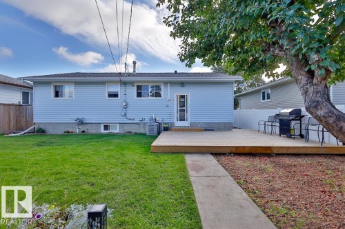 Expansive rear yard featuring a wooden deck, a concrete pathway, and a mature tree - 13312 123A Street Nw, Edmonton, AB 