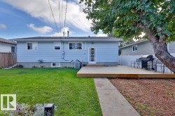 Expansive rear yard featuring a wooden deck, a concrete pathway, and a mature tree - 