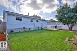 Expansive backyard featuring a manicured lawn, a raised wooden deck, a mature tree, and a white privacy fence - 