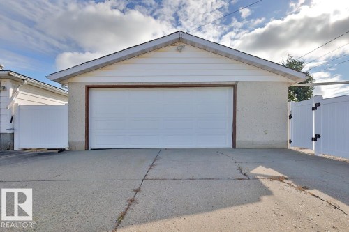 Detached garage with a white panel door, light-colored siding, and a gabled roofline - 13312 123A Street Nw, Edmonton, AB 