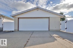 Detached garage with a white panel door, light-colored siding, and a gabled roofline - 