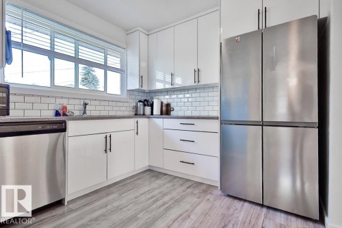 White kitchen cabinetry with matte black hardware, subway tile backsplash, stainless steel appliances, and wood-finish flooring - 13312 123A Street Nw, Edmonton, AB 