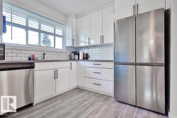 White kitchen cabinetry with matte black hardware, subway tile backsplash, stainless steel appliances, and wood-finish flooring - 