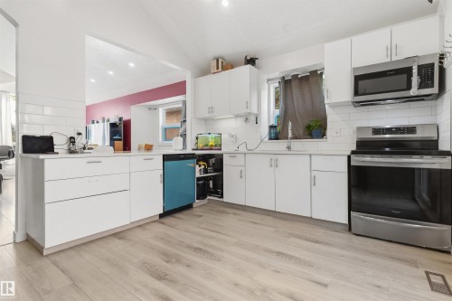 White cabinetry with brushed nickel hardware, light wood-finish flooring, white subway tile backsplash, stainless steel range, and built-in microwave - 4824 13 Avenue Nw, Edmonton, AB 