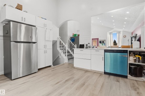 White cabinetry with stainless steel appliances, wood-finish flooring, and arched entryway - 4824 13 Avenue Nw, Edmonton, AB 