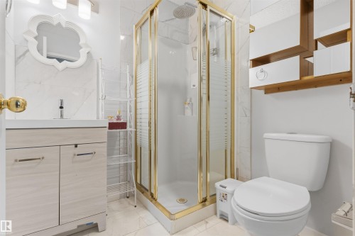 White vanity with integrated sink, gold-framed glass shower enclosure, white wall-mounted toilet, and wood-finish wall shelving - 4824 13 Avenue Nw, Edmonton, AB 