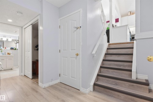 Wood-finish flooring, staircase with matching wood-finish treads, white painted walls, and interior doors with brass-finish hardware - 4824 13 Avenue Nw, Edmonton, AB 
