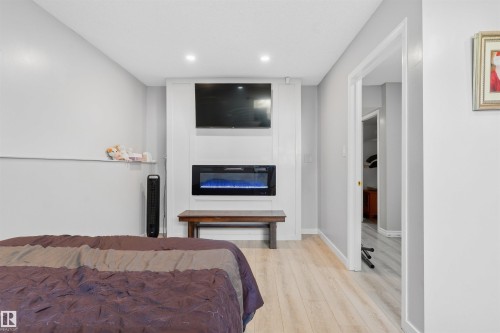 Integrated electric fireplace with a white surround, recessed lighting, and wood-finish flooring - 4824 13 Avenue Nw, Edmonton, AB 