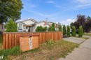 Wood fence with address display, mature landscaping, paved driveway, and covered front porch - 4824 13 Avenue Nw, Edmonton, AB 