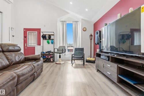 Vaulted ceiling with recessed lighting, wood-finish flooring, accent wall, red entry door with glass insert, and built-in media console - 4824 13 Avenue Nw, Edmonton, AB 