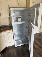 New refrigerator, cream-toned cabinetry with dark hardware, dark wood-finish flooring, and dark countertop - 